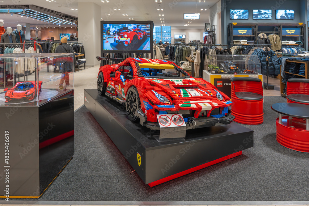 Naklejka premium Germany Berlin December 3, 2025. Large LEGO Ferrari race car is showcased in the menswear department. Colorful brick model draws attention amid racks of clothing.