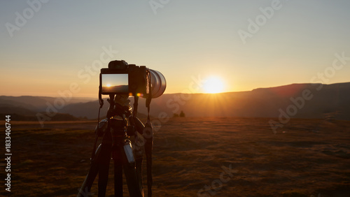 Landscape photography. A camera on a tripod against a backdrop of mountains in the last rays of the setting sun.