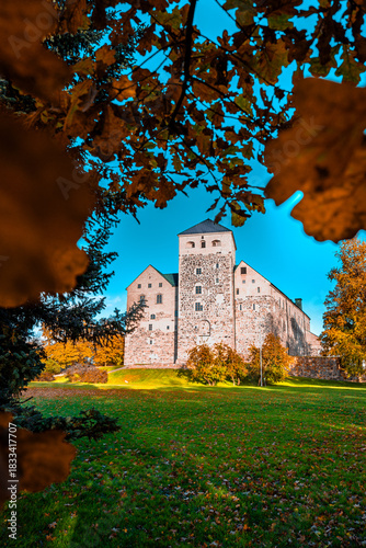 Vertical Photograph of Historic Turku Castle Surrounded by Vibrant Autumn Foliage.