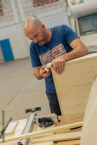 A young craftsman restores a caravan in a hangar.