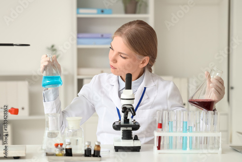 Female scientist with flasks and microscope working at table in laboratory