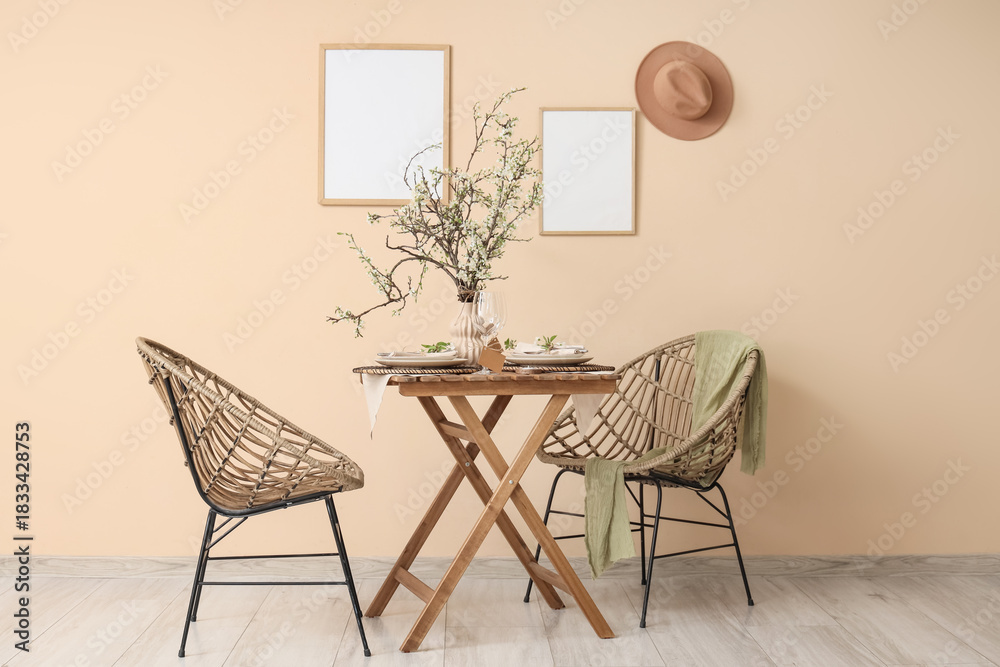 Fototapeta premium Elegant table setting with plates, glasses and blooming tree branches near beige wall