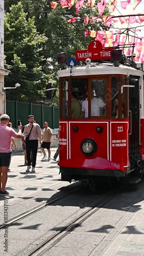 Istanbul, turkey, august 1, 2025 famous nostalgic red tramway traveling along a decorated istiklal avenue. Sunny day in istanbul, turkey with people walking on the street. Slow motion. Vertical format