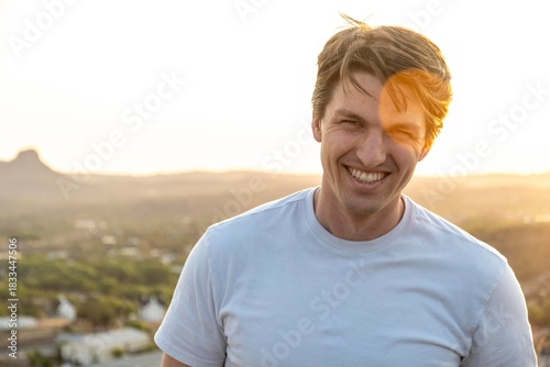 A man in a white shirt smiles while standing on a hill