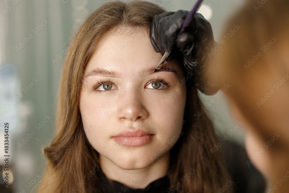 Fototapeta premium Young woman with beautiful eyebrows being styled by a skilled beauty artist in a serene salon environment