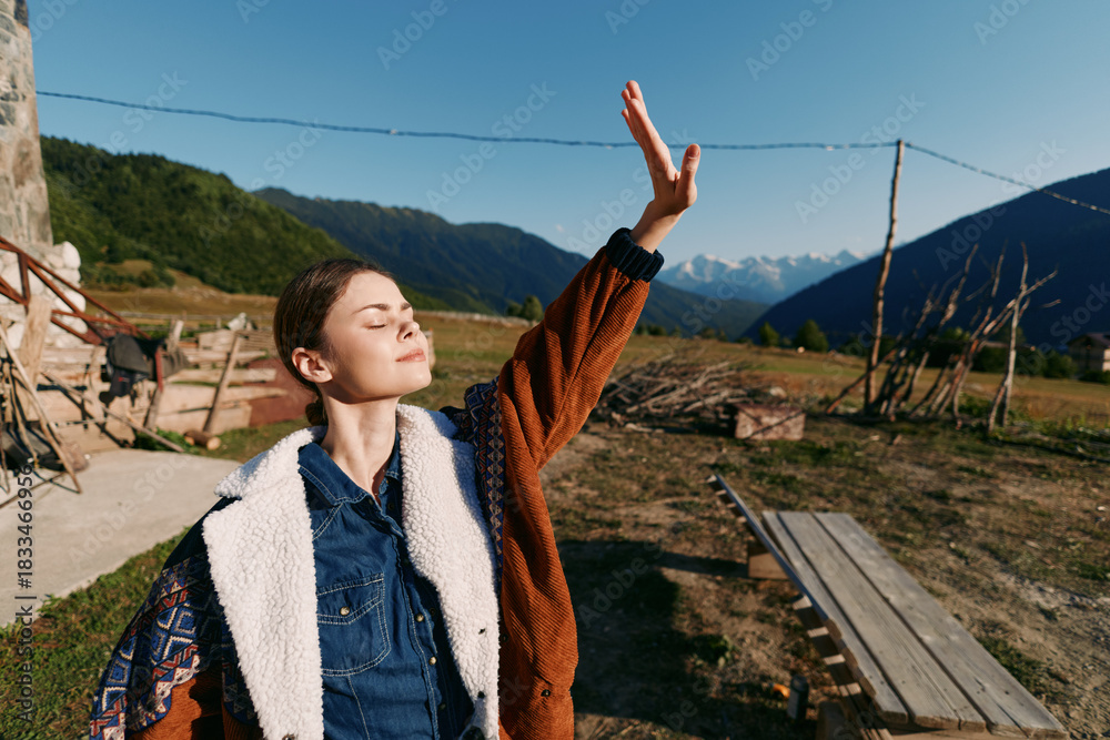 Fototapeta premium woman nature mountains sunlight outdoors portrait rural freedom enjoying fresh air with closed eyes and raised hand on a sunny day at a country farmhouse landscape for relaxation and wellbeing