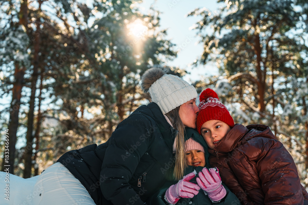 Obraz premium Happy loving family of mother and two daughters enjoying a sunny winter day in a snowy forest, wearing warm winter clothes, expressing tenderness and affection