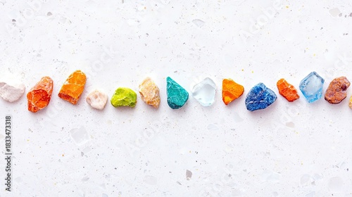 A line of colorful rocks on a white textured surface, creating a vibrant and eye-catching composition.