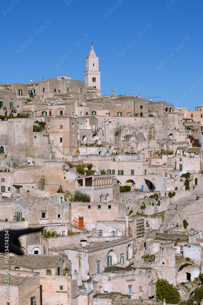 Fototapeta premium vertical shot of the iconic Sassi di Matera cityscape, unesco world heritage site in Basilicata, Italy, featuring the majestic cathedral bell tower.