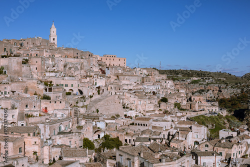 Obraz na plátne panoramic view of matera's sassi, an unesco world heritage site, featuring historic cave dwellings and the iconic bell tower under a bright blue sky