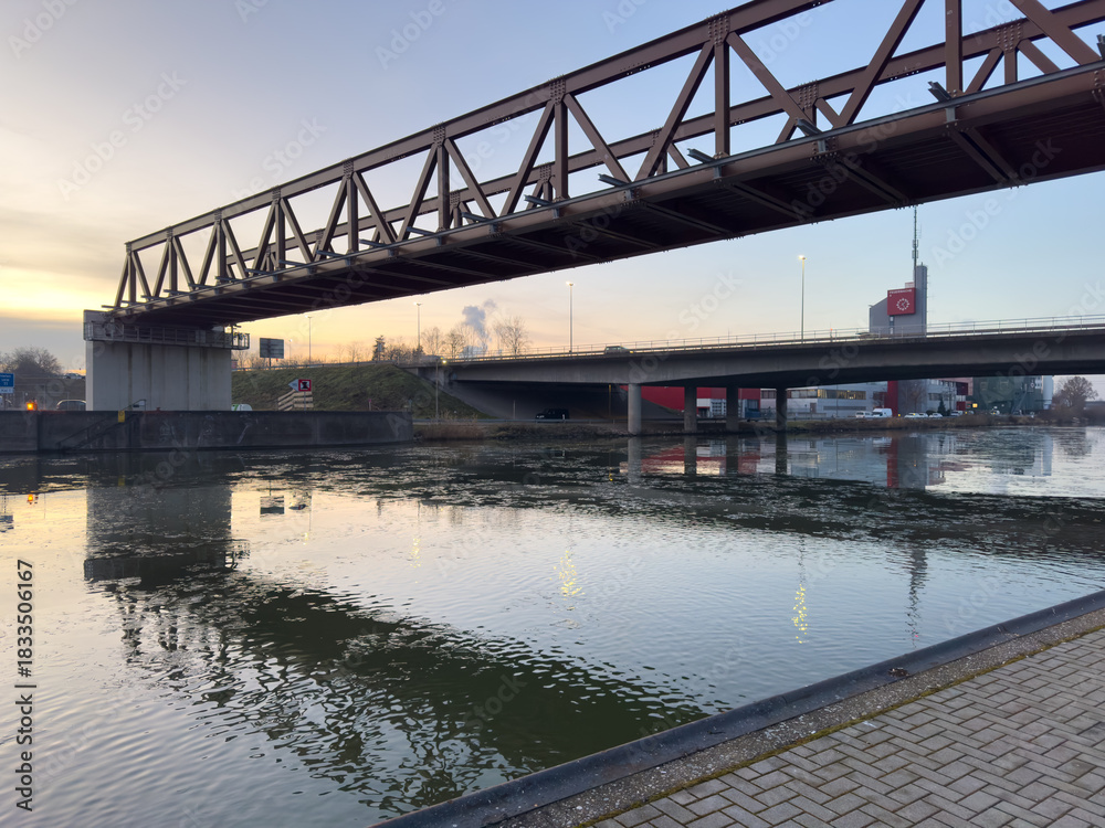 Obraz premium Truss bridge over urban canal reflecting sunset light