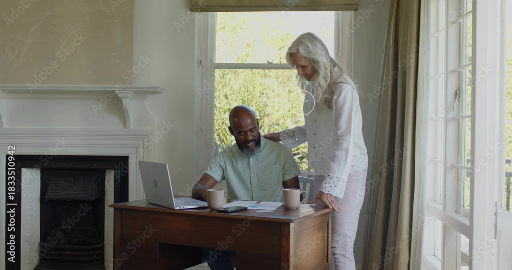 Fototapeta premium Reviewing couple leaning over desk at home in white blouse, green shirt, with laptop and papers