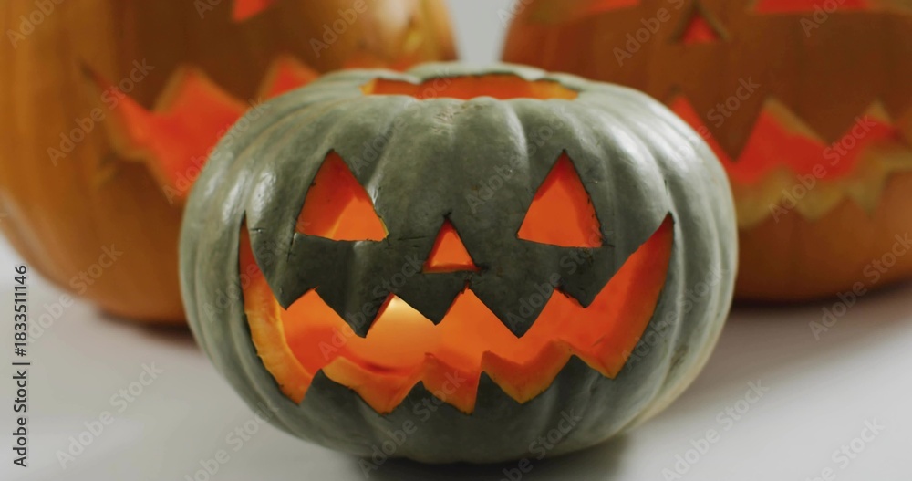 Fototapeta premium Glowing carved green pumpkin resting on white tabletop, showing cut edges, stems, internal lights