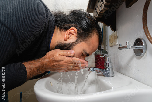 Slika na platnu Colombian man rinsing face with water at bathroom sink during personal hygiene routine