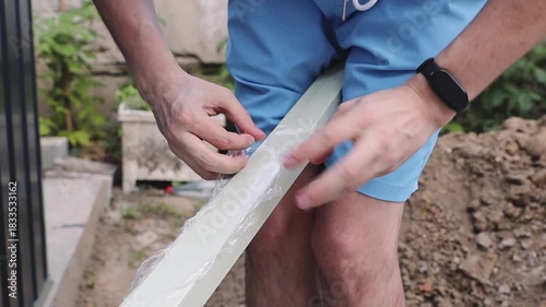 An installer unpacks a long white piece from film before installing a metal shed.