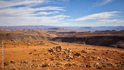 Wallpaper Mural Vast rugged panorama of the arid Atlas Mountains landscape in Morocco, featuring striking red-orange rocks, deep dry valleys, and a wide blue sky with streaky clouds Torontodigital.ca