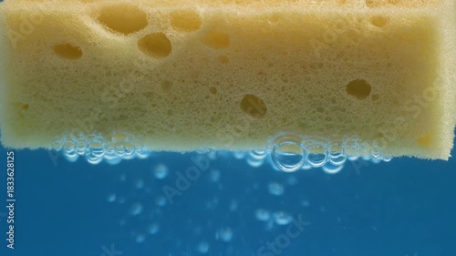 Sponge in water with bubbles rising, close-up view of cleaning tool.