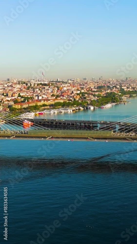 Vertical video. Istanbul, Turkey. Golden Horn Bridge and Halic Metro Station with pedestrian crossing illuminated by morning sun over bay. Aerial View, MasterShots, Dronie. Rich colors