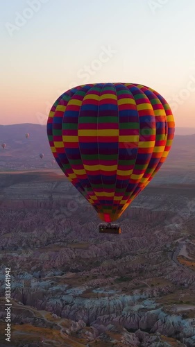 Vertical video. Goreme, Nevsehir, Turkey. Large colorful checkered hot air balloon with basket in backlight against the rising sun at dawn over Cappadocia. Aerial View, Point of interest. Rich colors