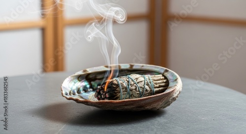 Smoldering sage bundle in iridescent abalone shell with rising smoke on gray surface