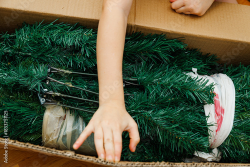 Child’s hand reaching into a cardboard box with artificial Christmas tree branches