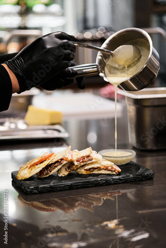 Gloved chef pouring molten cheese over crostini — saucier finishing touch