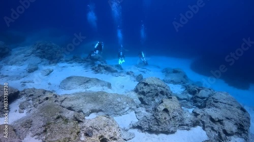 Group of scuba divers swimming in the ocean, sandy seabed with rocks, blue water. Ocean and scuba divers, underwater exploration video. Tourists in the sea.