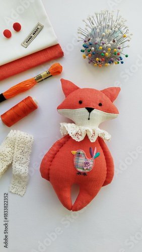 Overhead composition with orange plush fox, threads, scissors, lace and pins, cozy handmade mood