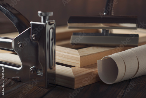 Rolled canvas and stretcher bars with tensioning tool in soft focus.