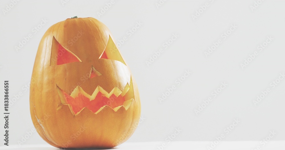Naklejka premium Glowing carved pumpkin sitting on white tabletop in studio, casting soft shadow, copy space