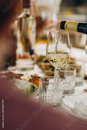 Hand pouring white wine into glass at dinner