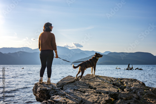 Woman and dog enjoying peaceful lake view and mountains at sunset
