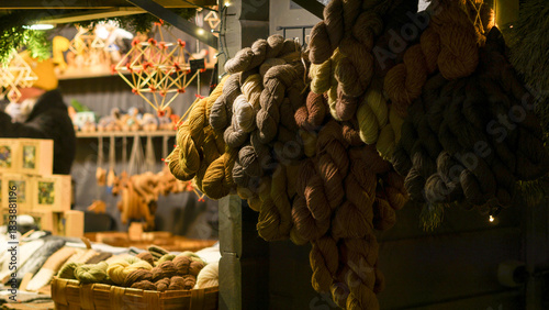 Natural dye skeins of yarn hang in a dimly lit Christmas market, alongside festive Christmas decorations. A cozy, handmade vibe with warmth, and artisanal charm. Festive shopping 