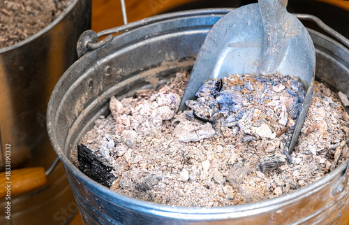 Close up of fireplace ash in a metal bucket with a scoop