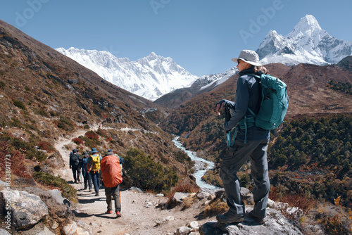 Female hiker watches group of backpackers on trail walking along river with Ama Dablam mountain in Himalayas, Nepal.