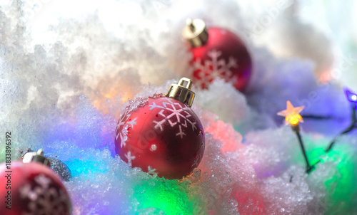 closeup on red Christmas balls with snowflake shaped in the snow and colorful lights of garland for holidays celebration