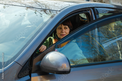 Mature woman at steering wheel of parked car with open driver door, checking surroundings before maneuvering