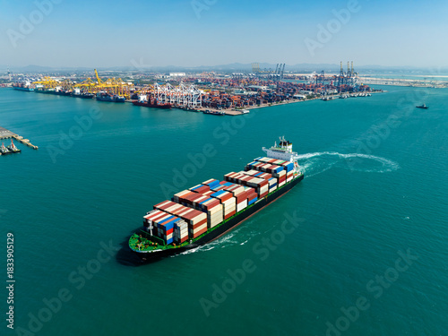 Aerial view of container ship approaching busy industrial port terminal hub for economy