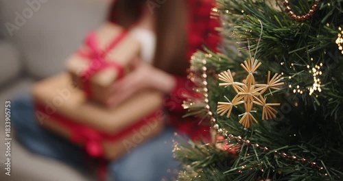 A person holds wrapped gifts near a decorated Christmas tree, creating a festive holiday scene. A person is holding a wrapped present with a red ribbon in front of a Christmas tree