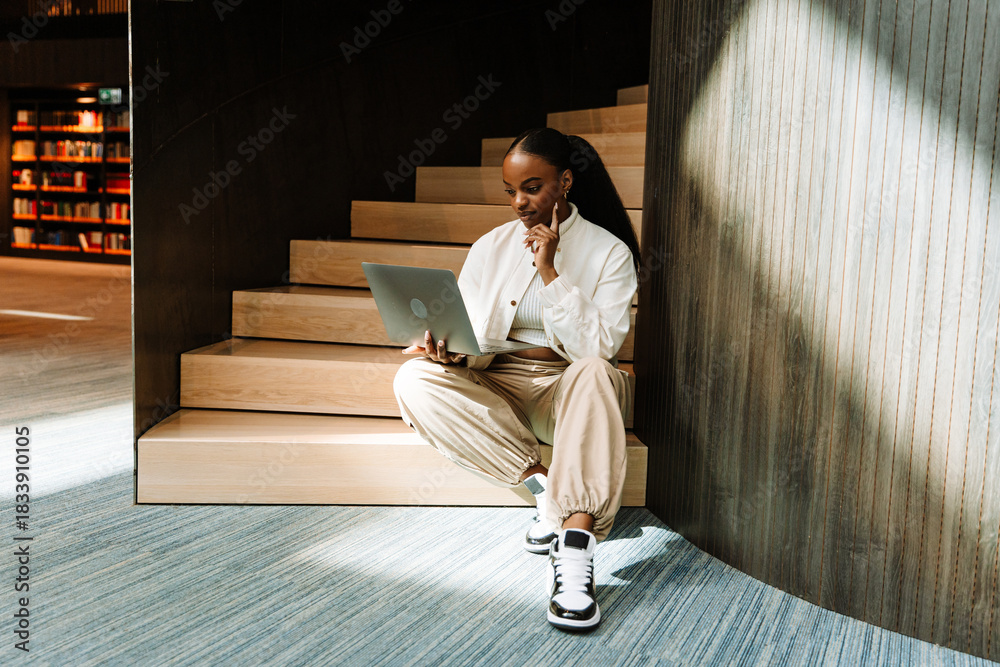 Fototapeta premium Female student looking at laptop while sitting on stairs