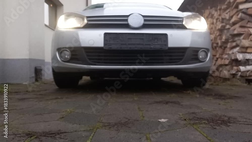 Engine ignition sound from front view of stationary car with headlights on at dusk near wooden stacks