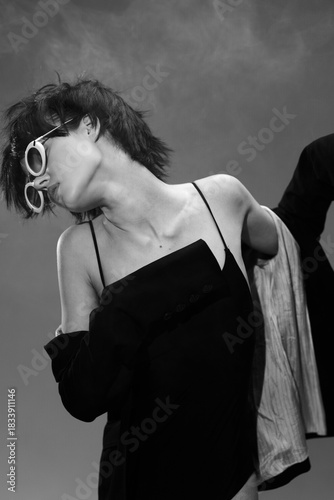 Black and white artistic portrait of a stylish woman wearing sunglasses and a strapless dress with a dramatic pose and moody background