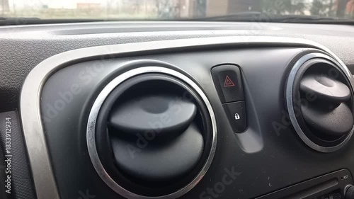 Close up view of car dashboard vents with hazard light button and flashing reflections visible