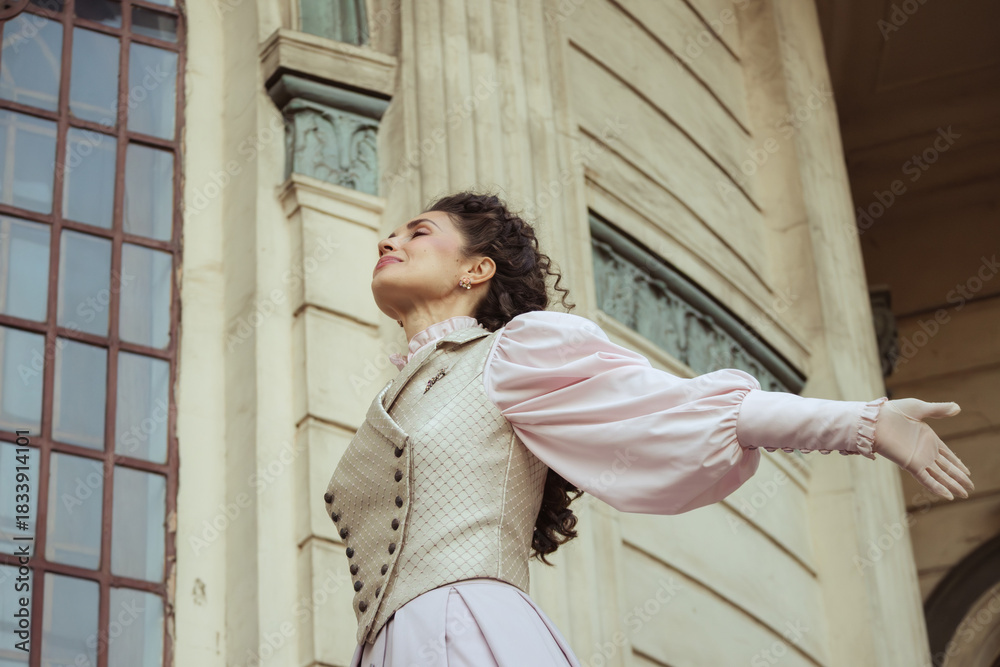 Fototapeta premium An elegant woman in a vintage dress stands by an old stone column
