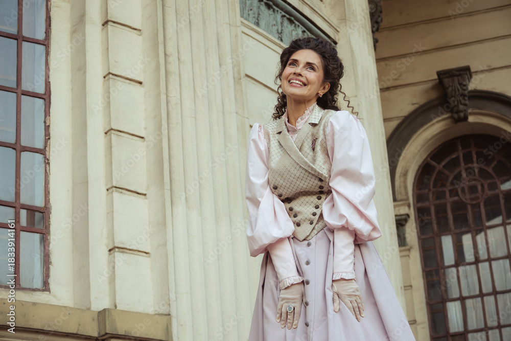 Fototapeta premium An elegant woman in a vintage dress stands by an old stone column