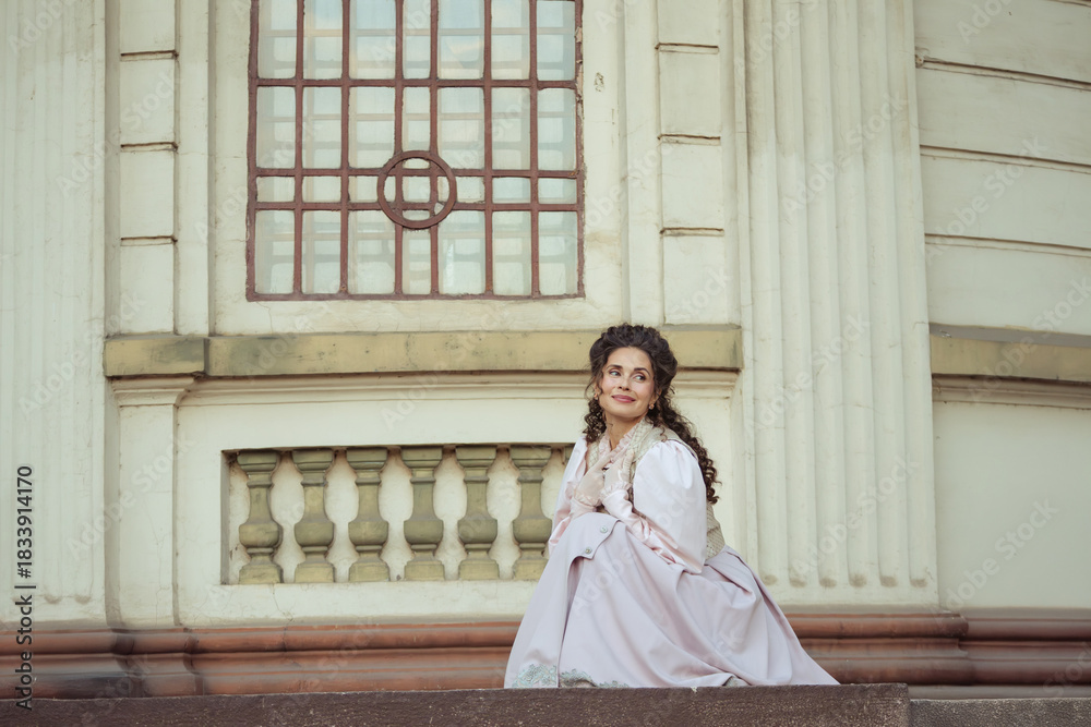 Fototapeta premium An elegant woman in a vintage dress stands by an old stone column
