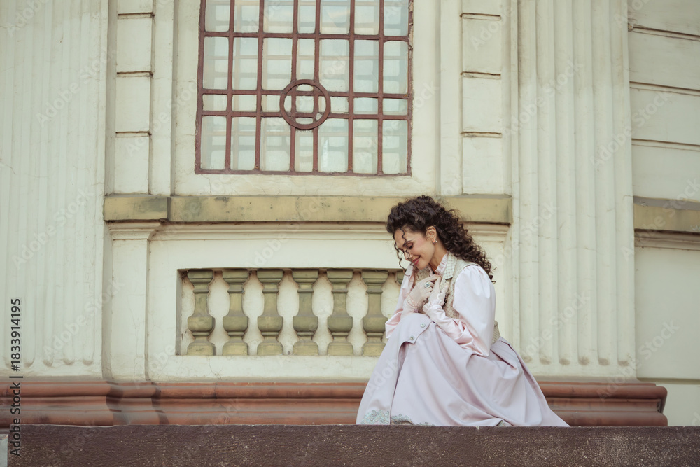 Fototapeta premium An elegant woman in a vintage dress stands by an old stone column