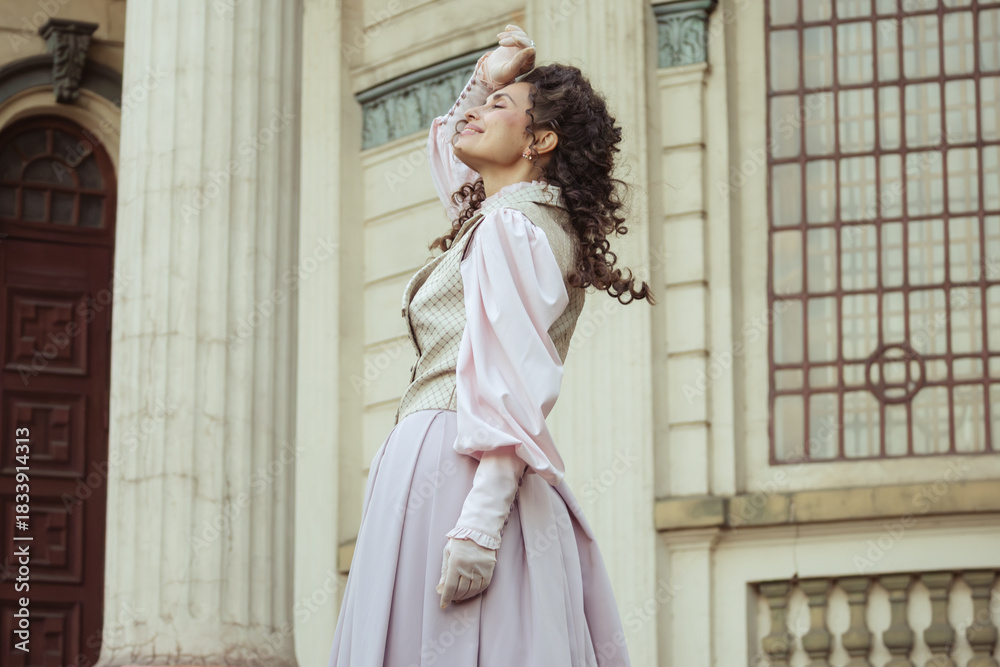 Fototapeta premium An elegant woman in a vintage dress stands by an old stone column