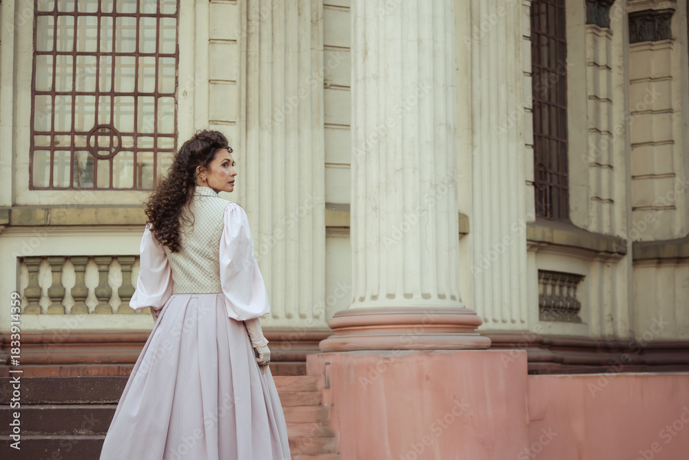 Fototapeta premium An elegant woman in a vintage dress stands by an old stone column