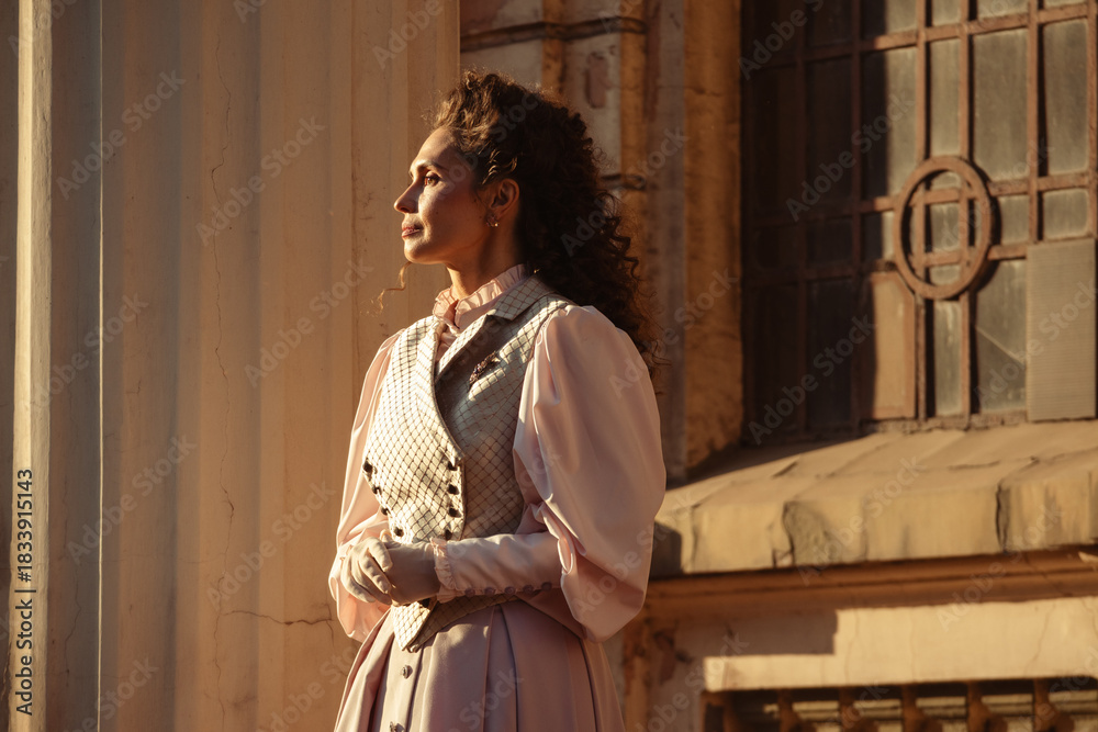 Fototapeta premium An elegant woman in a vintage dress stands by an old stone column